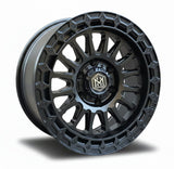 Load image into Gallery viewer, A matte black multi-spoke off-road wheel rim displayed in front of stacked cardboard boxes branded with the same logo.