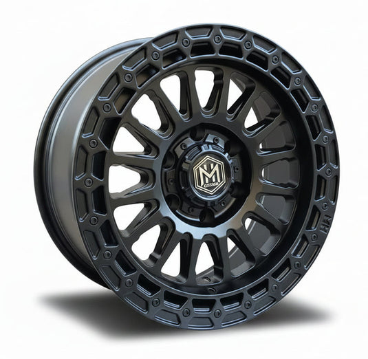 A matte black multi-spoke off-road wheel rim displayed in front of stacked cardboard boxes branded with the same logo.